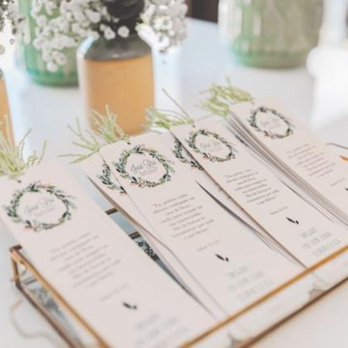 A close-up of a display of elegant wedding invite bookmarks in a tray, with floral arrangements in the background.