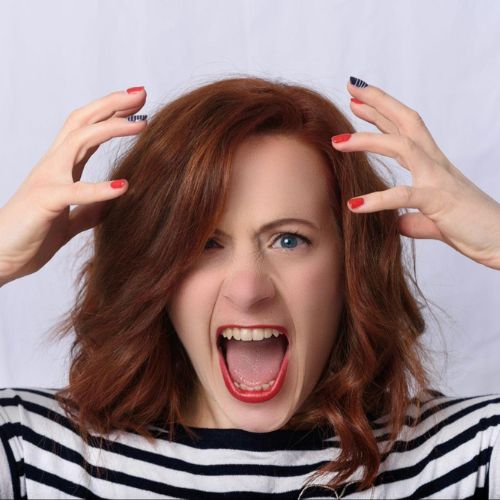 A woman with red hair and a striped shirt, appearing very frustrated and screaming