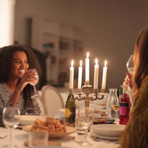 Two friends sitting at a beautifully set dinner table with a candelabra and enjoying a meal together while drinking wine.