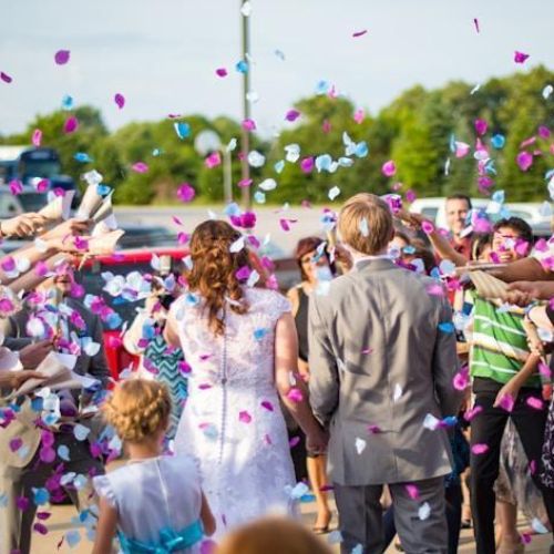 A bride and groom walking away from a crowd of guests who are showering them with colorful confetti during a wedding celebration.