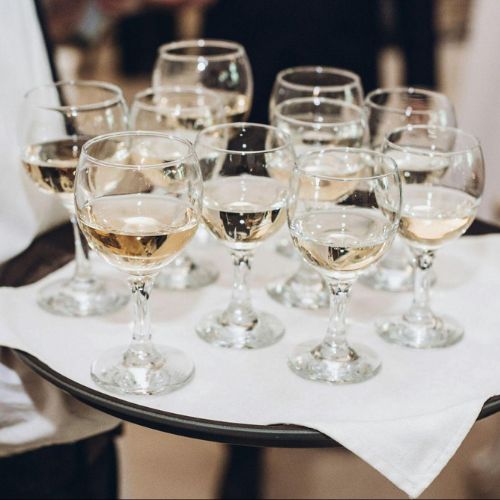 A tray filled with multiple glasses of white wine, arranged neatly and ready to be served at an event.
