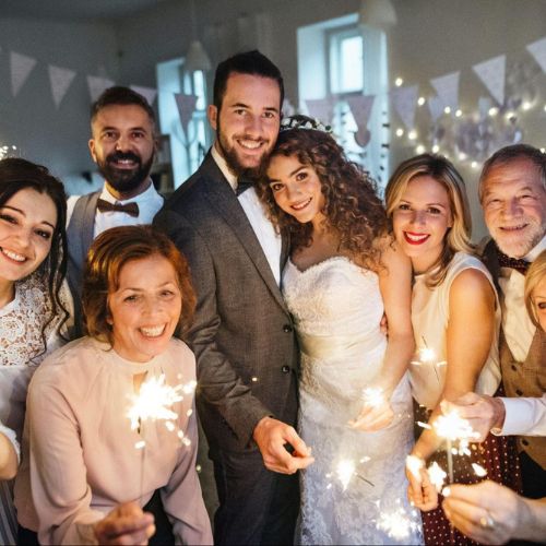 A group of people celebrating at a wedding, including the bride and groom in the center. Everyone is holding sparklers and smiling.