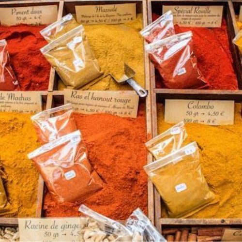 A colorful display of various ground spices in bags and piles. Each spice is labeled with its name and price.