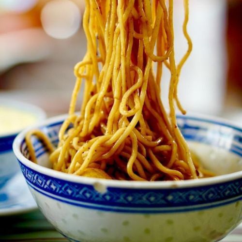 A close-up view of cooked noodles being lifted from a bowl with chopsticks.