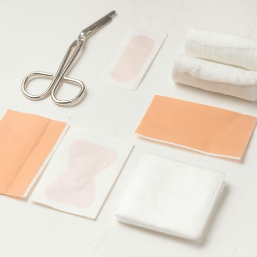 A flat lay of medical supplies on a white surface, including scissors, gauze, and various adhesive bandages.