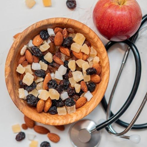 A wooden bowl filled with a mix of almonds, raisins, and dried pineapple chunks on a light surface