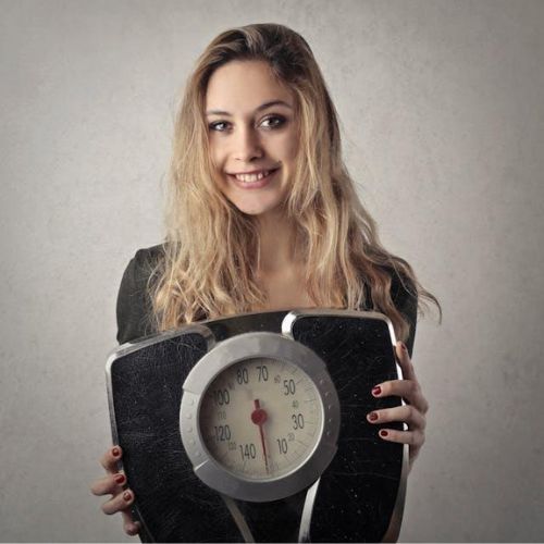 A young woman holding a large mechanical bathroom scale in front of her