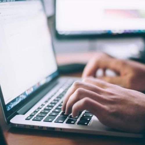 A close-up of someone's hands typing on a laptop keyboard