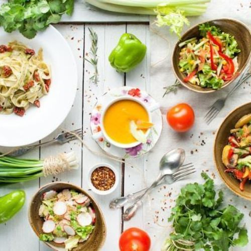 Healthy vegan spread on the table that includes salads, pasta with tofu, pumpkin soup, tomatoes, peppers and green onion 