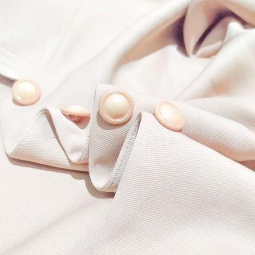 A close-up of a cream-colored garment showing detailed tailoring with three elegant, round pearl buttons on a folded collar.