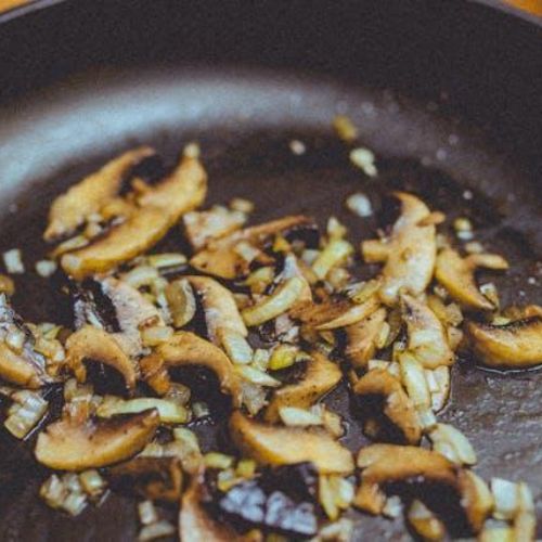 A close-up image of a frying pan with sautéed thinly sliced mushrooms and finely chopped onions