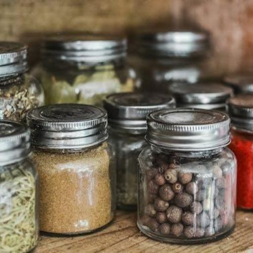 A collection of small glass jars with metal lids containing various dried spices and herbs