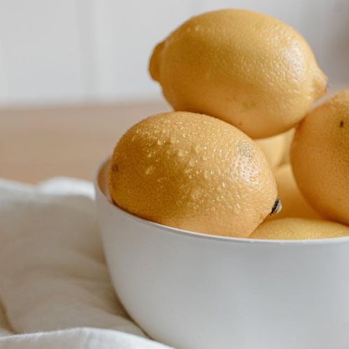 A white bowl filled with bright yellow lemons, resting on a wooden surface