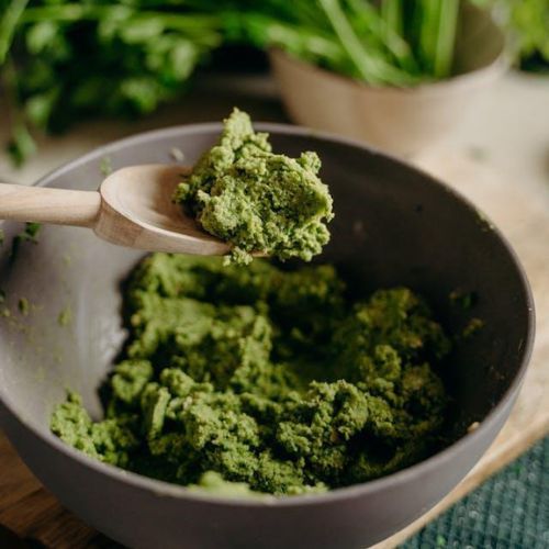 A wooden spoon scooping up a portion of a green paste from a brown bowl.