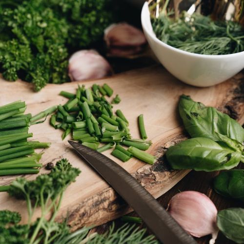 A wooden cutting board covered with fresh, chopped green herbs, including parsley, chives, and basil