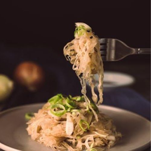 A fork lifting a portion of sauerkraut garnished with green onion from a plate.
