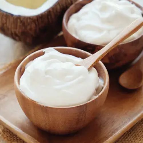 Two wooden bowls of coconut cream with a spoon, placed on a wooden tray with a rustic background, symbolizing vegan dairy alternatives.