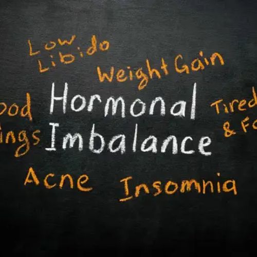 Blackboard with orange chalk text listing symptoms of hormonal imbalance like mood swings, acne, and insomnia.