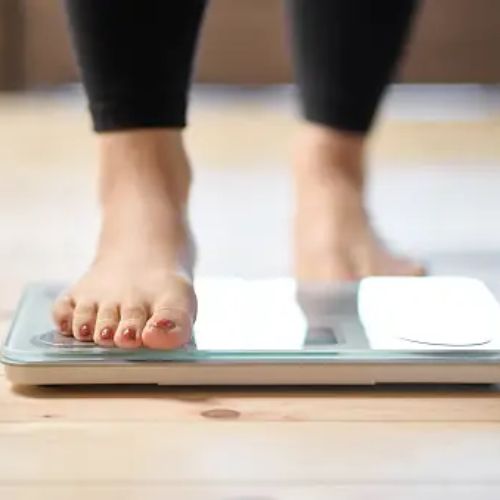 A close-up of a woman's feet stepping onto a digital bathroom scale, focused on weight measurement