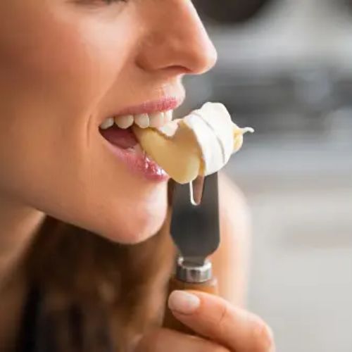 A woman eating a forkful of cheese, capturing a moment of enjoyment while eating it.