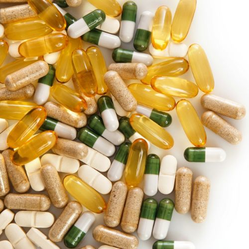 An assortment of dietary supplements spread out, including yellow fish oil capsules, green and white capsules, and various tablets, emphasizing health and wellness through supplementation.