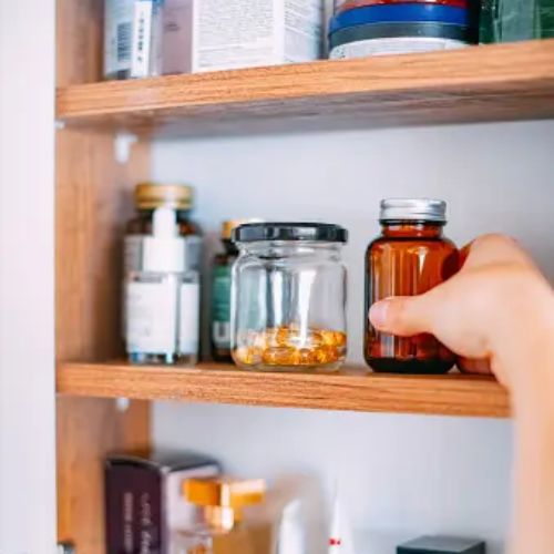 A hand reaching for a medicine bottle inside a well-stocked home medicine cabinet, suggesting self-care or health management.