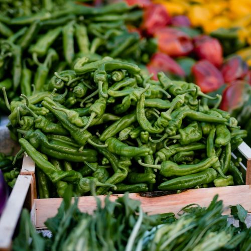 Freshly harvested curly green peppers piled high in a market setup, showcasing the diversity of vegetables available for culinary uses.