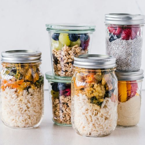 A variety of healthy food ingredients including grains, fruits, and vegetables neatly packed into mason jars, illustrating organized meal prep and storage.