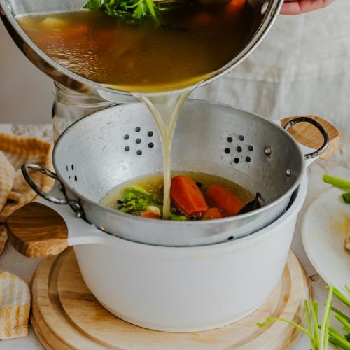 Pouring homemade vegetable broth through a strainer into a pot, capturing the process of making nutritious soup with fresh ingredients.