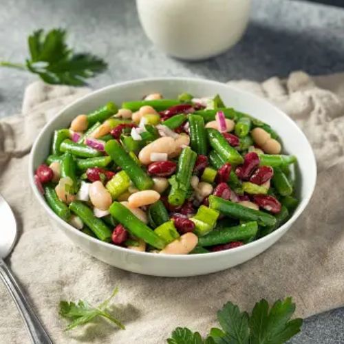 A healthy green bean and bean salad, served in a round white bowl on a table, garnished with parsley.