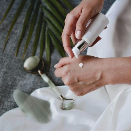 A close-up of hands applying lotion or cream with a jade roller and skincare tools in the background