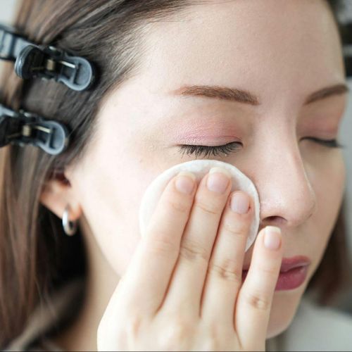 A close-up of a woman’s face as they use a makeup pad or cotton round on their cheek