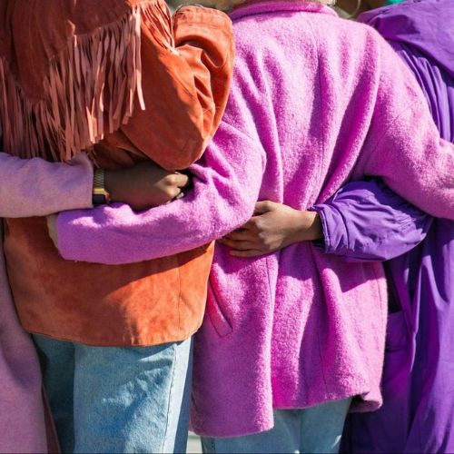 A group of woman standing with their arms around each other, wearing colorful jackets