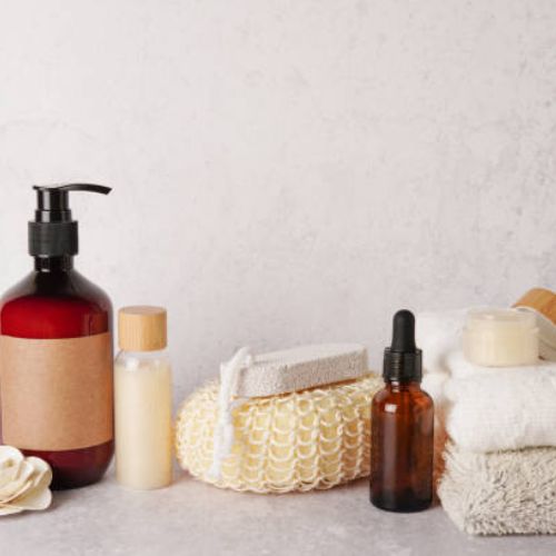 A collection of bath and skincare products including a pump bottle, small containers, a loofah, and folded towels