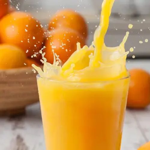 A splash of fresh orange juice being poured into a glass, with whole oranges in the background