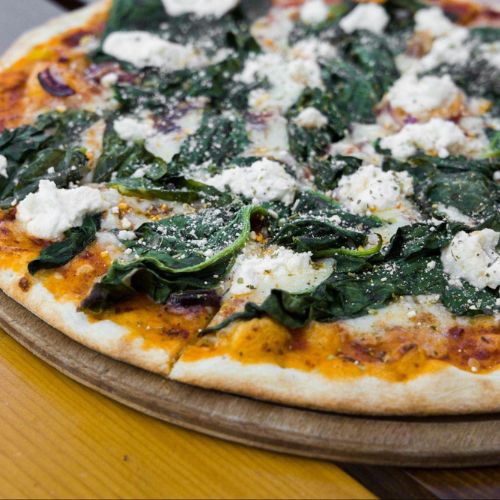 A vegetarian pizza topped with spinach and ricotta cheese on a wooden board