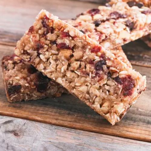 Two granola bars with nuts and dried fruit on a wooden table