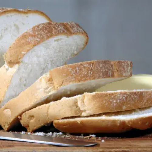 Sliced white bread loaf with a knife and a slab of butter on a wooden cutting board