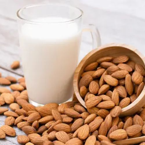 A glass of almond milk surrounded by scattered almonds on a wooden table