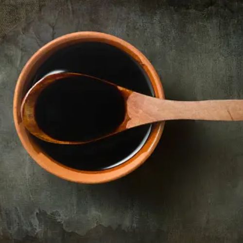 A wooden spoon resting in a bowl of thick dark soy sauce