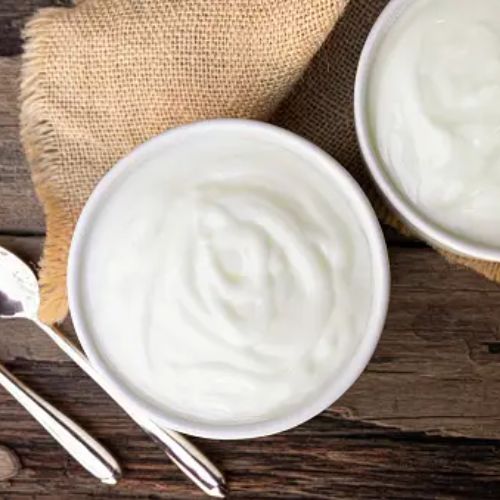 Two bowls of plain yogurt on a wooden surface with silver spoons