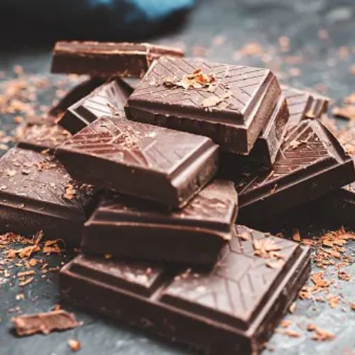 A stack of dark chocolate pieces with chocolate shavings scattered around