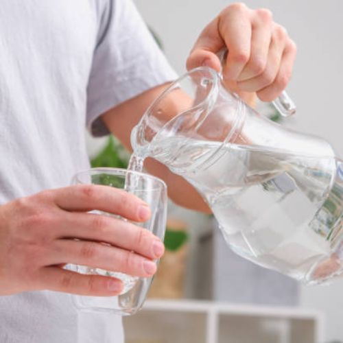 A man pouring water from a clear glass pitcher into a glass