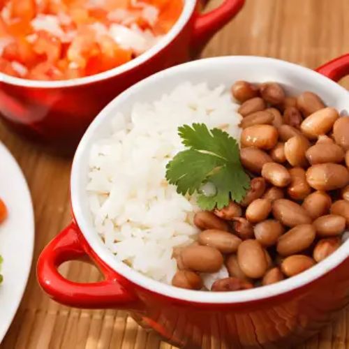 A close-up of a plate with rice and beans garnished with cilantro, with a side of fresh vegetables and salsa in the background