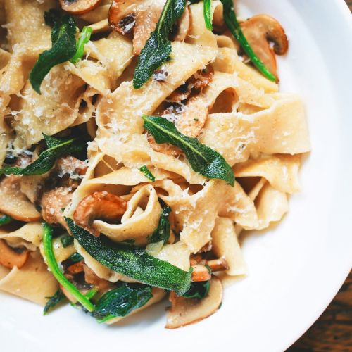 A plate of pasta with mushrooms, spinach, and grated cheese, garnished with fresh herbs, on a white plate.