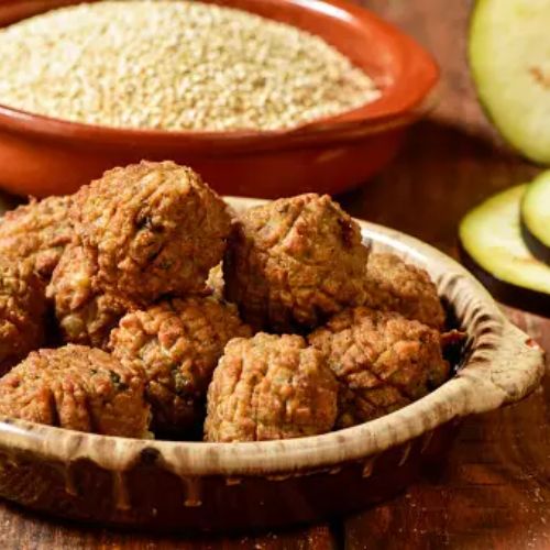 A bowl of homemade quinoa and eggplant fritters with a bowl of raw quinoa and slices of eggplant in the background