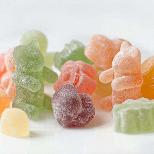 A close-up of various colorful, sugar-coated gummy candies arranged on a white surface.