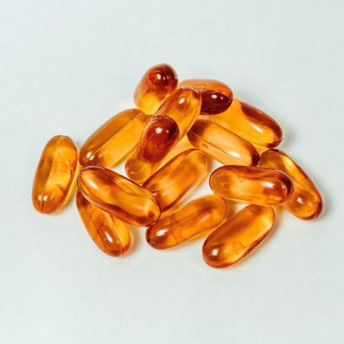 A group of softgel capsules with a shiny, amber appearance laid out on a white surface.