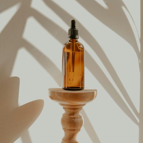 A small amber glass dropper bottle placed on a wooden stand, with soft shadows of leaves in the background creating an aesthetic and serene ambiance.