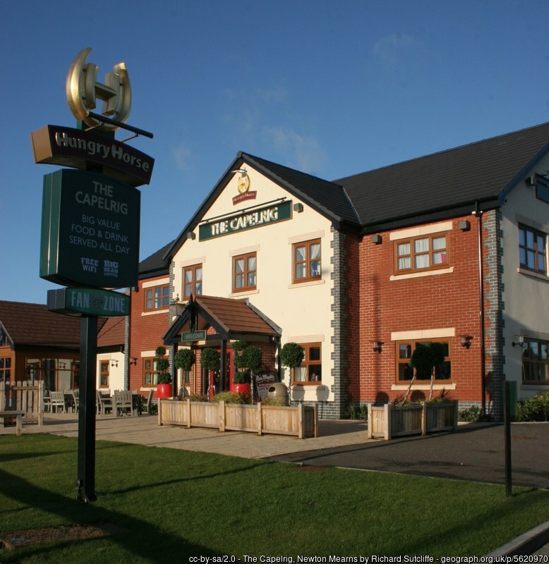 The image features The Capelrig, a pub under the Hungry Horse brand. The building has a mix of brick and cream-coloured walls with a traditional, welcoming facade. A prominent sign in front advertises "Big Value Food & Drink Served All Day," alongside the Hungry Horse logo. The outdoor seating area is arranged with planters and chairs, giving the pub a cosy atmosphere under a clear blue sky.